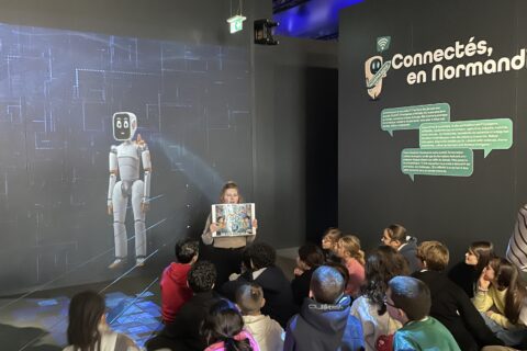 une classe de primaire à l'entrée de l'exposition Destination IA avec une animatrice